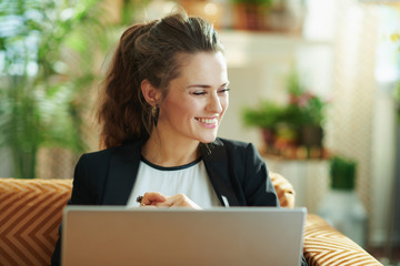happy stylish female using laptop while sitting on sofa