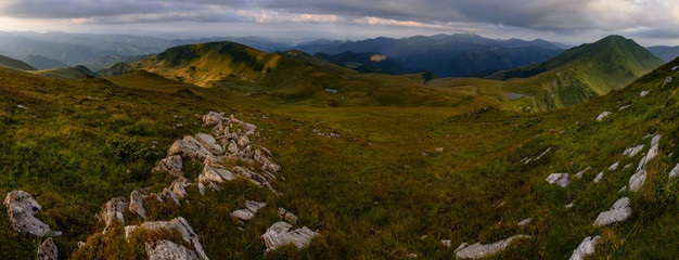 Fototapeta premium Wonderful springtime panoramic landscape in mountains at sunrise. Grassy slopes and forested hills illuminated with morning sunshine. Wild scenery. Farcau Peak. Maramures. Romania. Europe.