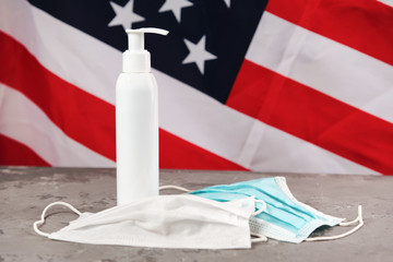 hand sanitizer alcohol pump without label for frequent washing and disinfection hands and two masks on concrete surface, american flag on background. Copy space