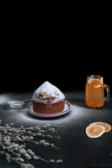 Easter cake with icing sugar on a dark background, sea buckthorn tea, slices of orange.