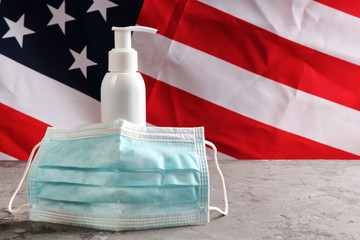 hand sanitizer alcohol pump without label for frequent washing and disinfection hands and used mask on concrete surface, american flag on background. Copy space