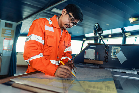 Filipino deck Officer on bridge of vessel or ship wearing coverall during navigaton watch at sea . He is plotting position on chart