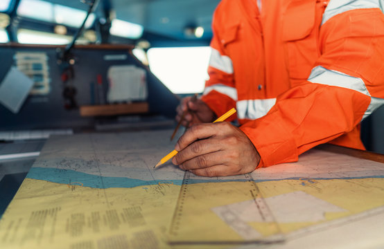 Filipino deck Officer on bridge of vessel or ship wearing coverall during navigaton watch at sea . He is plotting position on chart