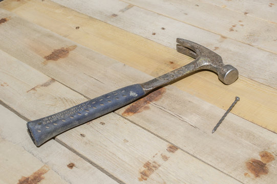 A blue handled 20 ounce hammer laying down beside a nail on a panel of old barn wood.