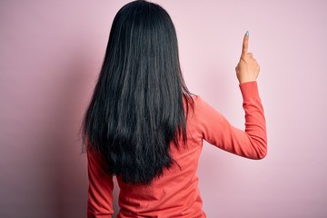 Young beautiful chinese woman wearing casual sweater over isolated pink background Posing backwards pointing ahead with finger hand
