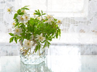 Forest flowers in a glass stand on the table against the background of white lace curtains.