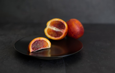 A slice of juicy ripe red bloody orange on a black plate against a black background.
