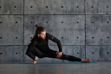 A young man with a beard practices yoga in the gym.