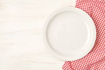 Empty plate with red napkin over white wooden table background.