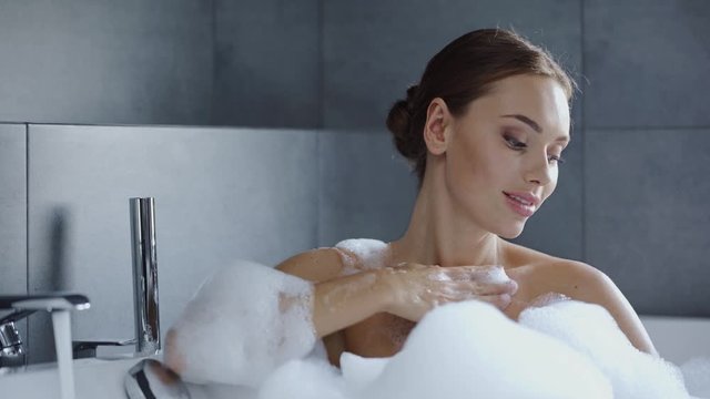 beautiful young woman washing in bath tub with foam