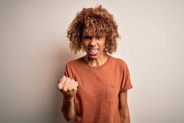 Fototapeta na wymiar Beautiful african american woman with curly hair wearing casual t-shirt over white background angry and mad raising fist frustrated and furious while shouting with anger. Rage and aggressive concept.
