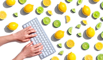 Woman using a computer keyboard with fresh lemons and limes overhead view - flat lay