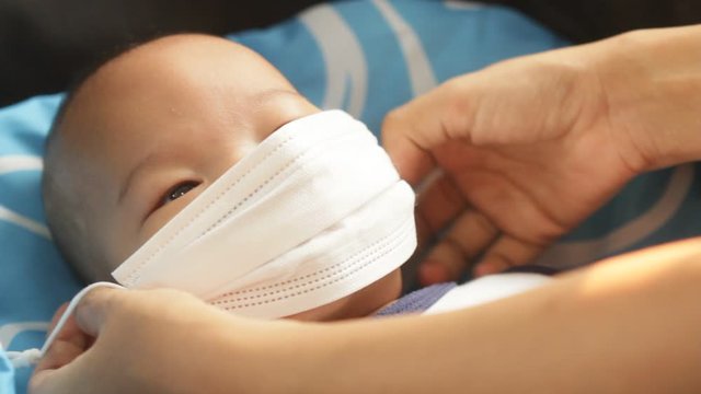mother putting on Protective mask to her son to protect from Corona virus or Covid-19 virus outbreak, Covid-19 Coronavirus concept. Virus and illness protection. newborn not good mood