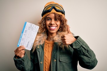 Young african american tourist woman wearing ski goggles holding plane boarding pass tickets happy...