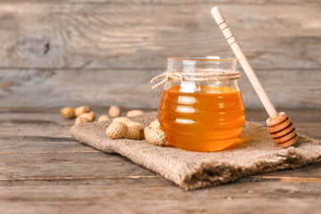Jar of sweet honey and peanuts on wooden background