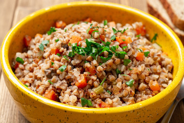 Buckwheat porridge with vegetables and mushrooms in ceramic bowl on rustic wooden table