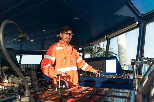 Filipino deck Officer on bridge of vessel or ship wearing coverall during navigaton watch at sea . He is maneuvering with cpp thrusters propulsion