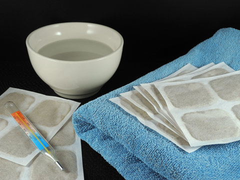 Mustard plasters on blue terry towel next to thermometer and bowl of water on black background. Warming of muscle tissues for chronic aches. Cold treatment.   