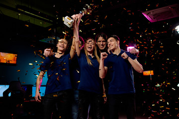 Winners of cybersports championship raising golden award while celebrating winning under falling confetti