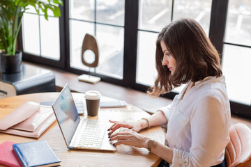 Business woman in white shirt working at laptop at home office, drinking coffee. Distance learning.Chat on mobile. Wooden table,organizer.Remote work place.Quarantine of coronovirus pandemic covid-19