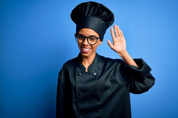 Young african american chef woman wearing cooker uniform and hat over blue background Waiving saying hello happy and smiling, friendly welcome gesture