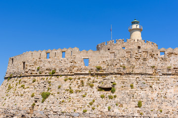 Wall with lighthouse of the fort of St. Nicholas in Mandrakia port of Rhodes. Greece