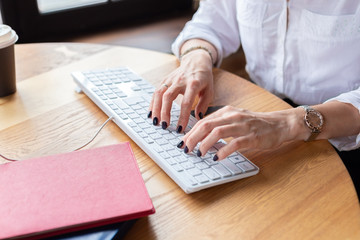 Business woman in white shirt typing on keyboard. Home office,drinking coffee.Distance learning.Hands, black manicure.Wooden table,organizer.Remote work place.Quarantine,coronovirus pandemic covid-19