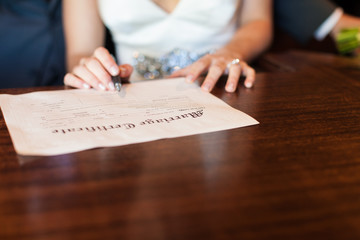 Bride holding pen signing marriage certificate