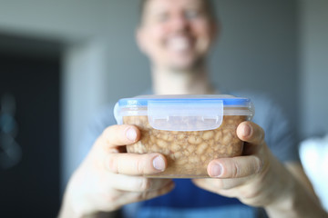 Close-up of smiling happy male worker holding plastic container with food. Macro shot of lunch. Break from work and snack. Handyman service and renovation concept