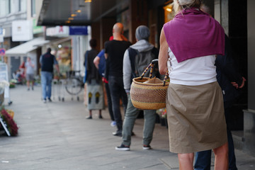 Low angle and selected focus, European people queue and wait for shopping on sidewalk outside...