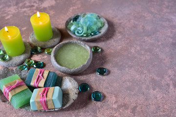 Fototapeta na wymiar Spa, zen and relaxation concept. Bath and aromatherapy accessories in stone bowl, handmade soap, shampoo and body cream. Burning candles and glass gems. Colors green, stone gray, yellow. 
