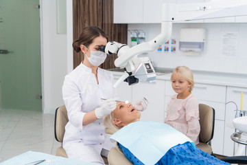 Obraz premium A blond woman having her teeth checked at the dentist's office, with her daughter waiting for her