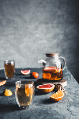 Citrus tea in a transparent teapot on a gray concrete background. Healthy drink, vegan, eco product.