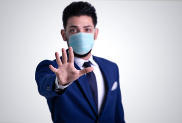 Young man with blue suit showing stop sign with hand, wearing  medical face mask. stop coronavirus concept.