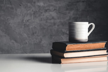 A cup of coffee on stack of books on grey background