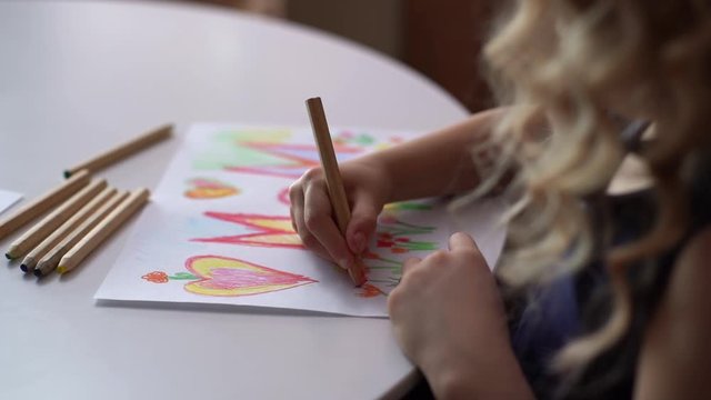 Rear view of adorable daughter drawing with colorful pencils on paper at home surprise for her mother at the table in cozy childs room. Concept of Happy Mothers Day. Tracking shot in slow motion.