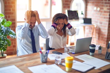 Middle age beautiful business workers working together using laptop at the office suffering from headache desperate and stressed because pain and migraine. Hands on head.