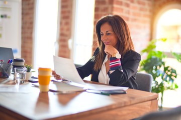 Middle age beautiful businesswoman smiling happy and confident. Sitting on chair working in a desk at the office