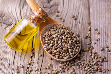 Heap of dried organic hemp seeds or cannabis plant seeds in spoon with glass of hemp seed oil on wooden backdrop. cannabis herb concept. hemp seed used birdseed