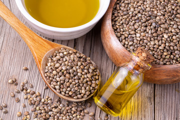 Heap of dried organic hemp seeds or cannabis plant seeds in spoon with glass of hemp seed oil on wooden backdrop. cannabis herb concept. hemp seed used birdseed