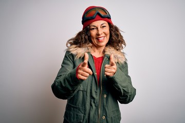Middle age skier woman wearing snow sportswear and ski goggles over white background pointing fingers to camera with happy and funny face. Good energy and vibes.