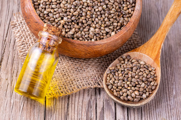 Heap of dried organic hemp seeds or cannabis plant seeds in spoon with glass of hemp seed oil on wooden backdrop. cannabis herb concept. hemp seed used birdseed