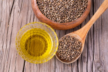 Heap of dried organic hemp seeds or cannabis plant seeds in spoon with glass of hemp seed oil on wooden backdrop. cannabis herb concept. hemp seed used birdseed