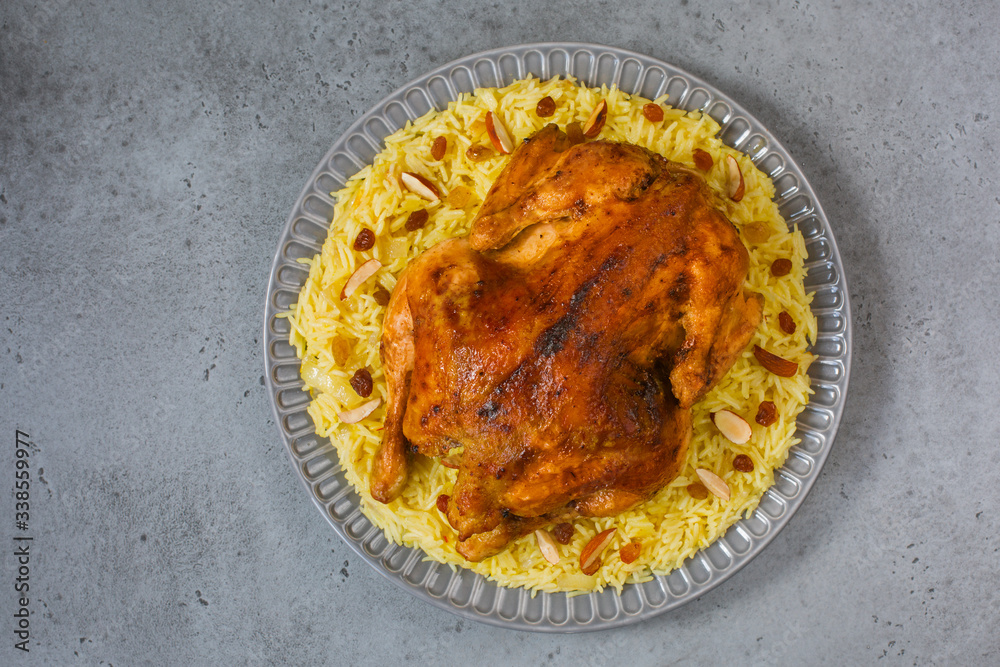 Poster Kabsa - arabian dish made of long grain basmati rice, whole chicken, onion, spices: cardamom, saffron, cinnamon, bay leaves.  Decorated with almonds and raisins. Saudi Arabia food.