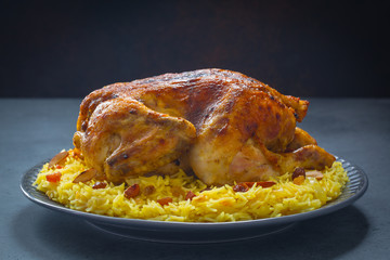 Kabsa - arabian dish made of long grain basmati rice, whole chicken, onion, spices: cardamom, saffron, cinnamon, bay leaves.  Decorated with almonds and raisins. Saudi Arabia food.