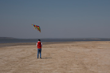 Obraz premium A 10 year old boy in a white sweatshirt and orange vest launches a kite on a deserted beach in solitude.