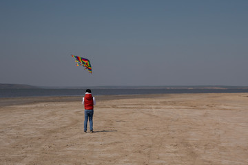 A 10 year old boy in a white sweatshirt and orange vest launches a kite on a deserted beach in solitude.
