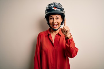 Middle age motorcyclist woman wearing motorcycle helmet over isolated white background pointing finger up with successful idea. Exited and happy. Number one.