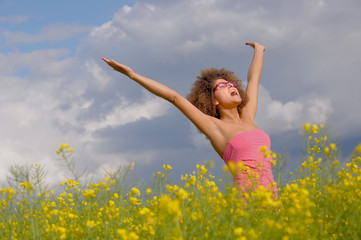 An attractíve young woman stands in a rapeseed field 
in springtime. She has a pink top on and wears trendy
pink glasses.  