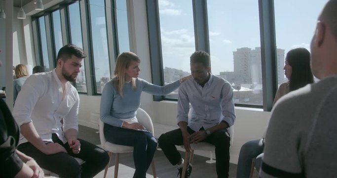 Pensive sad young african-american man tells his sad story of addiction to games surrounded by a mixed race of sympathetic people. Concept of getting rid of addiction with people who understand you